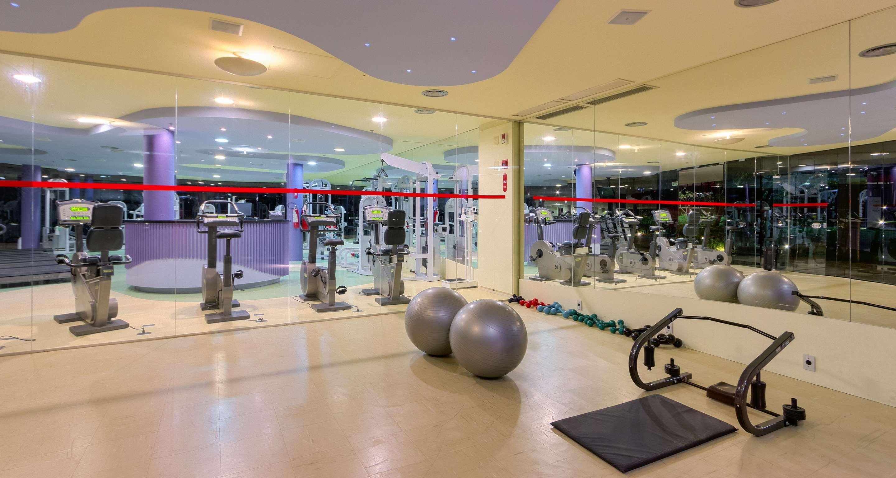 ホテル ロイヤル チューリップ ブラジリア アルボラーダ エクステリア 写真 The photo depicts a gym or fitness area. In the foreground, there are two large exercise balls and a mat on the floor. Behind them, there is a wall of mirrors that reflects various gym equipment, including exercise machines and bikes. The lighting in